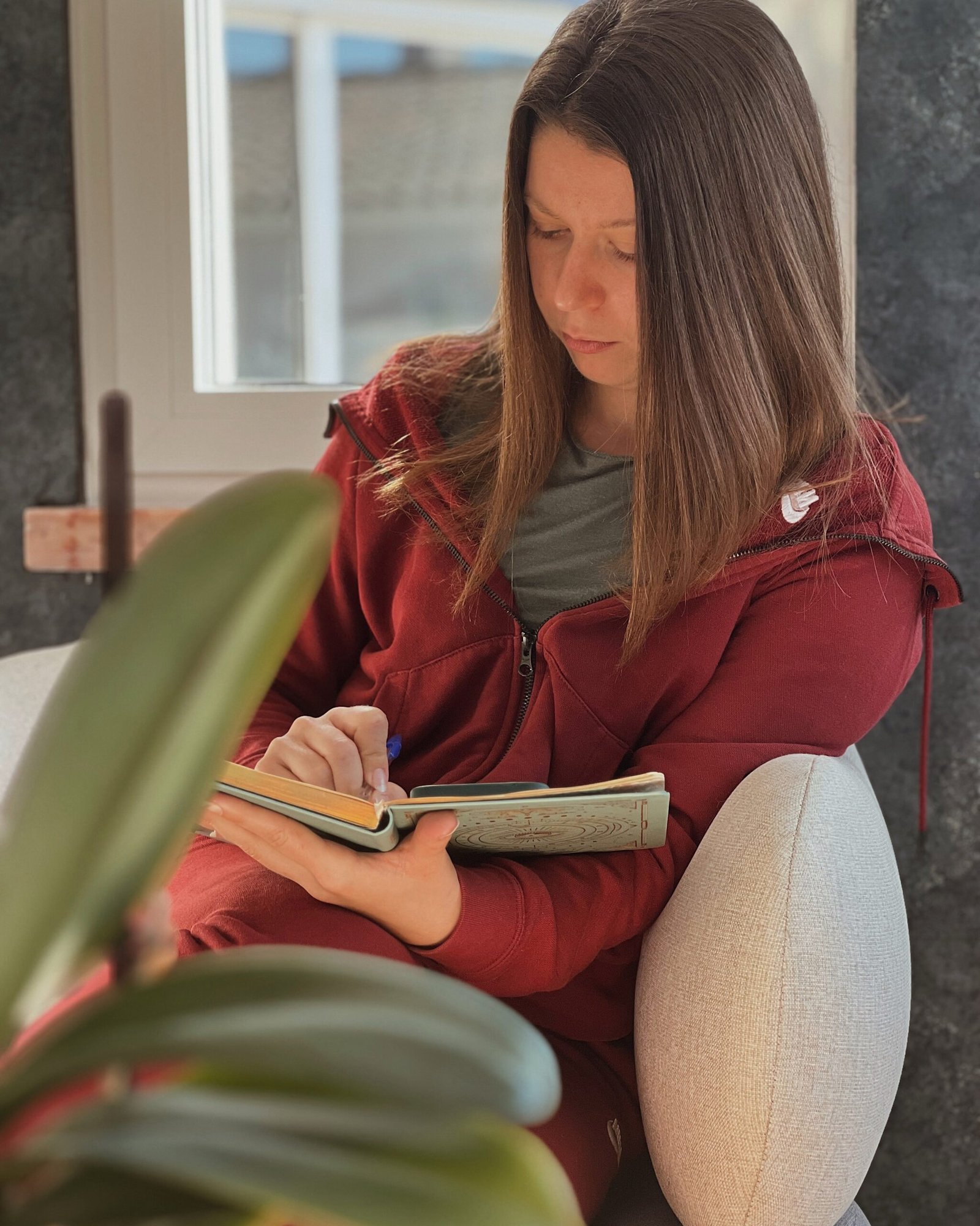 The photo portraits a woman sitting on the sofa, writing on a planner.